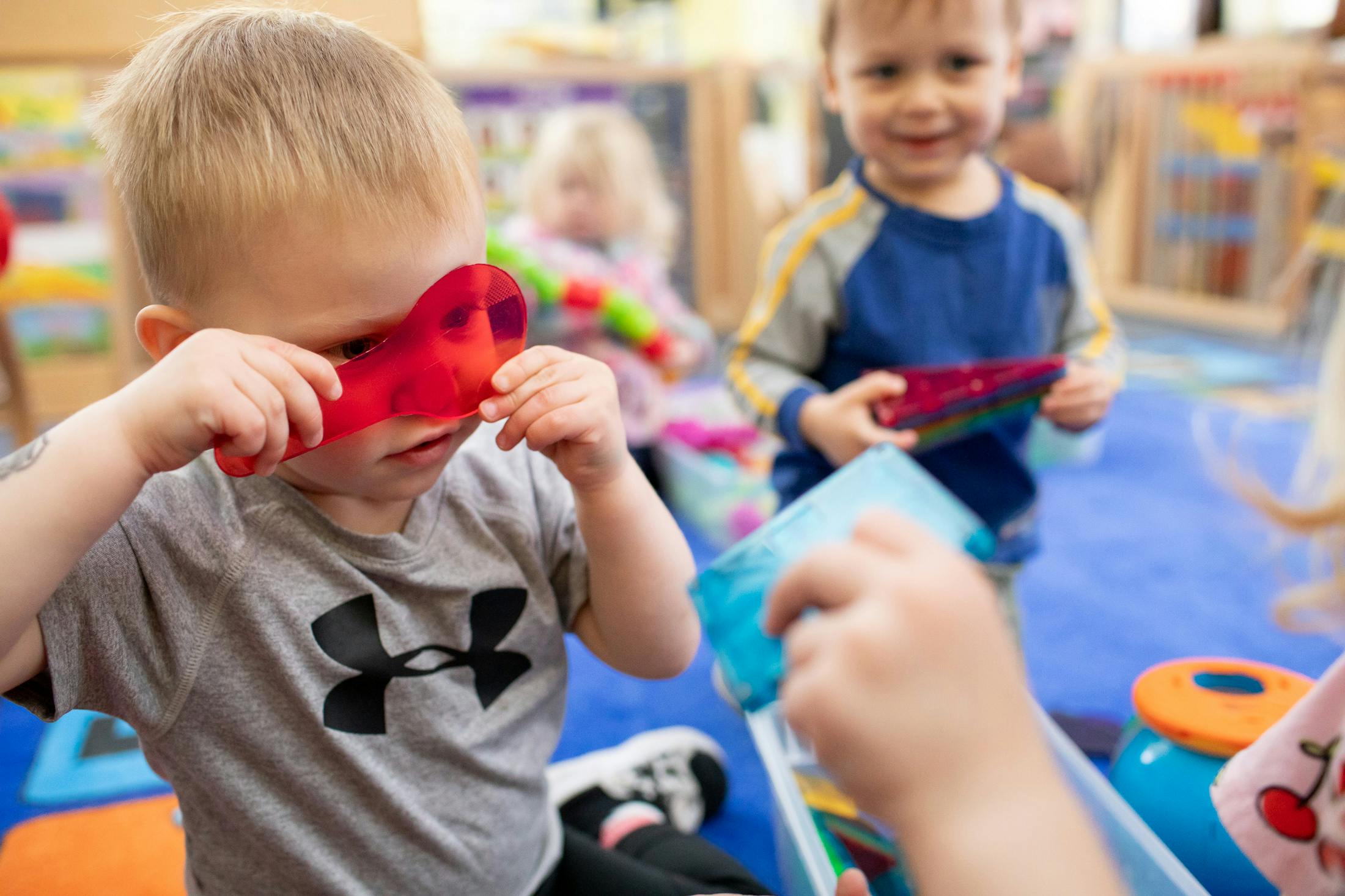 Child holding a red toy up to their eyes in a classroom