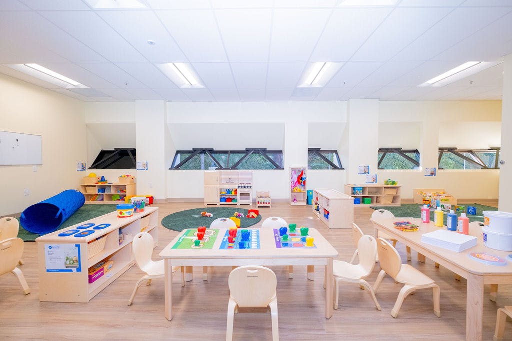 Empty classroom with small tables and chairs, play kitchen, and toys