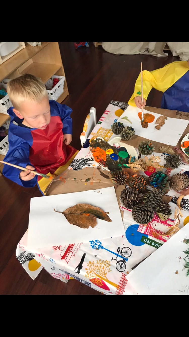 Child painting a leaf at a table with pinecones