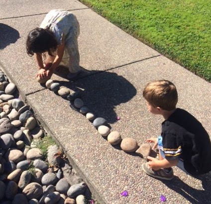 Two children arranging rocks in a line on a concrete surface