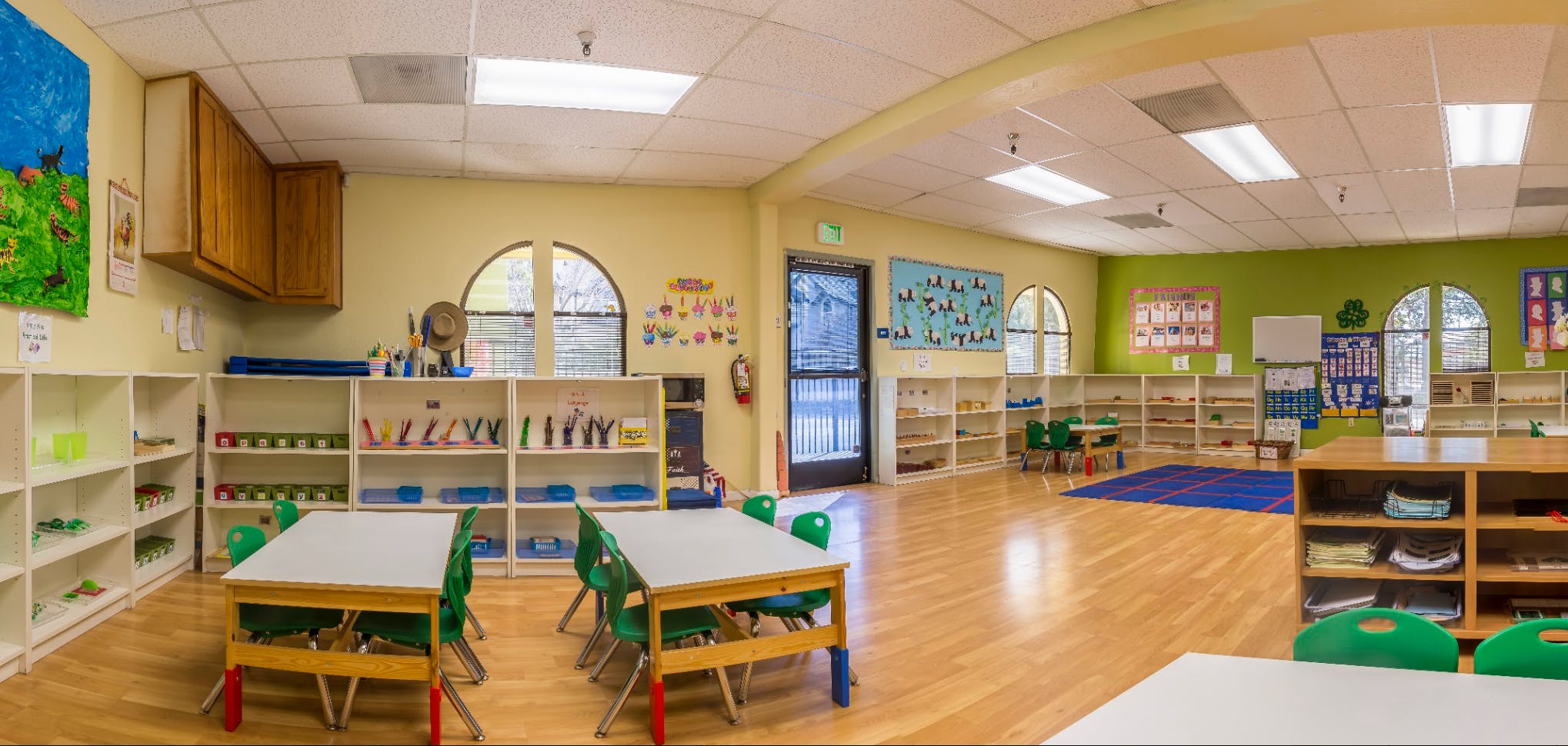Empty preschool classroom with small tables and chairs and shelves