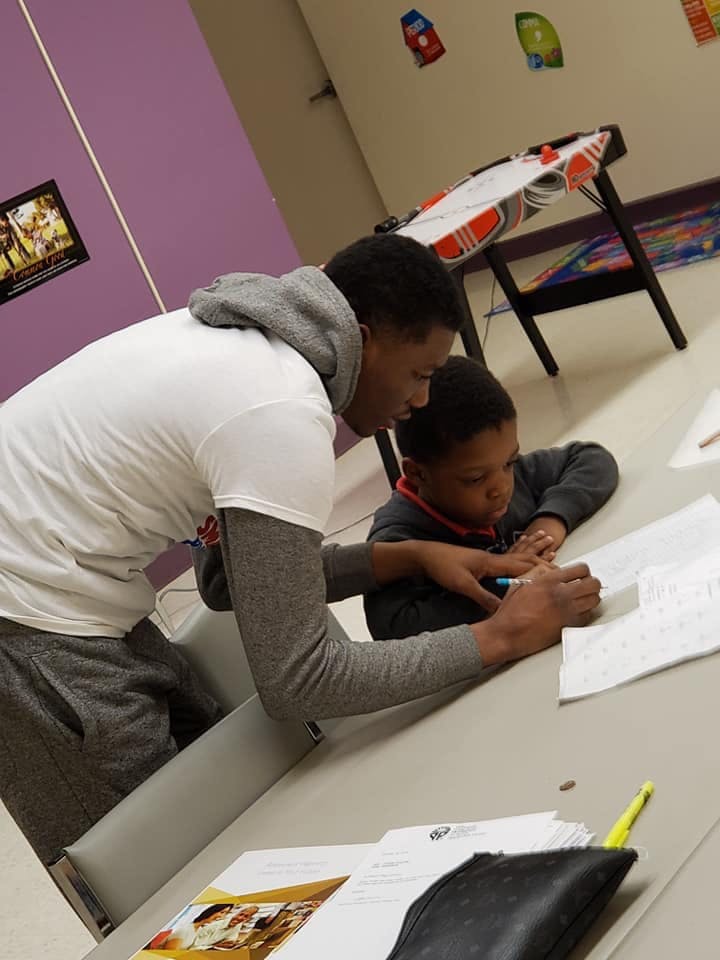 Person helping a child write at a table