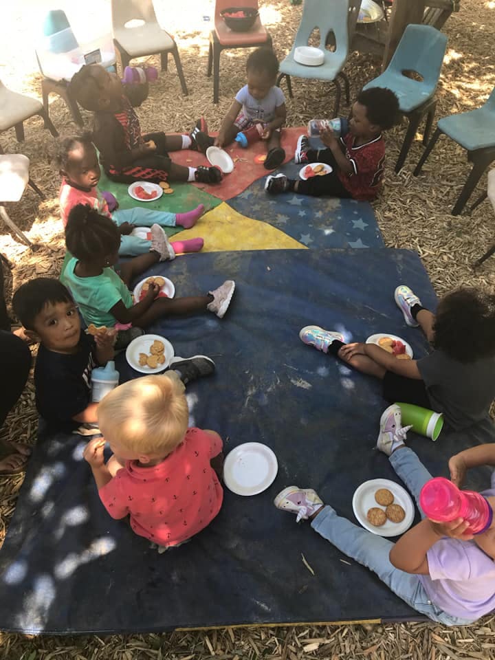 Children sitting on a mat eating snacks
