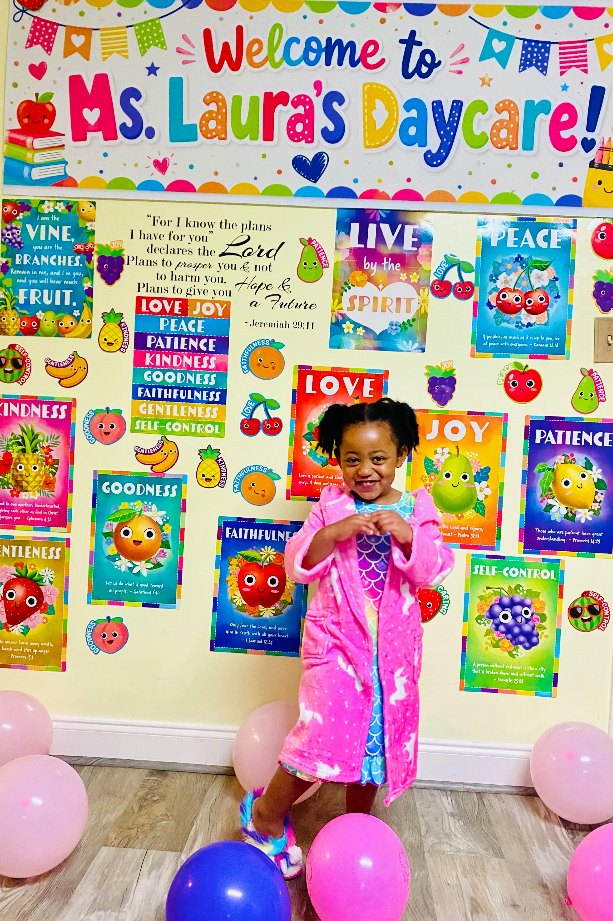 Child in a pink robe standing in front of a colorful daycare sign