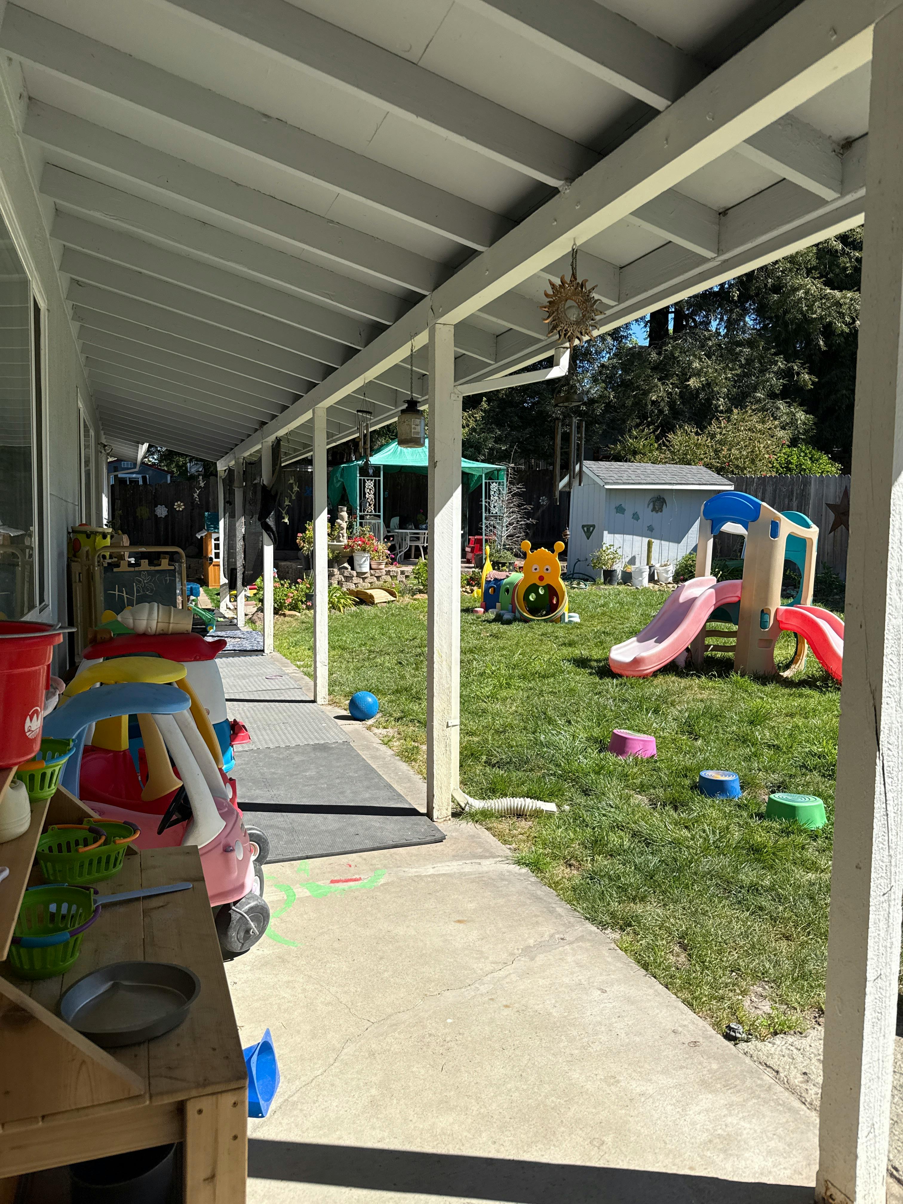 Playground with plastic slide, toys, and grass seen from under a patio