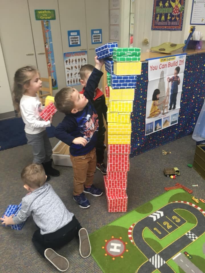 Children building a tall tower with large blocks in a classroom
