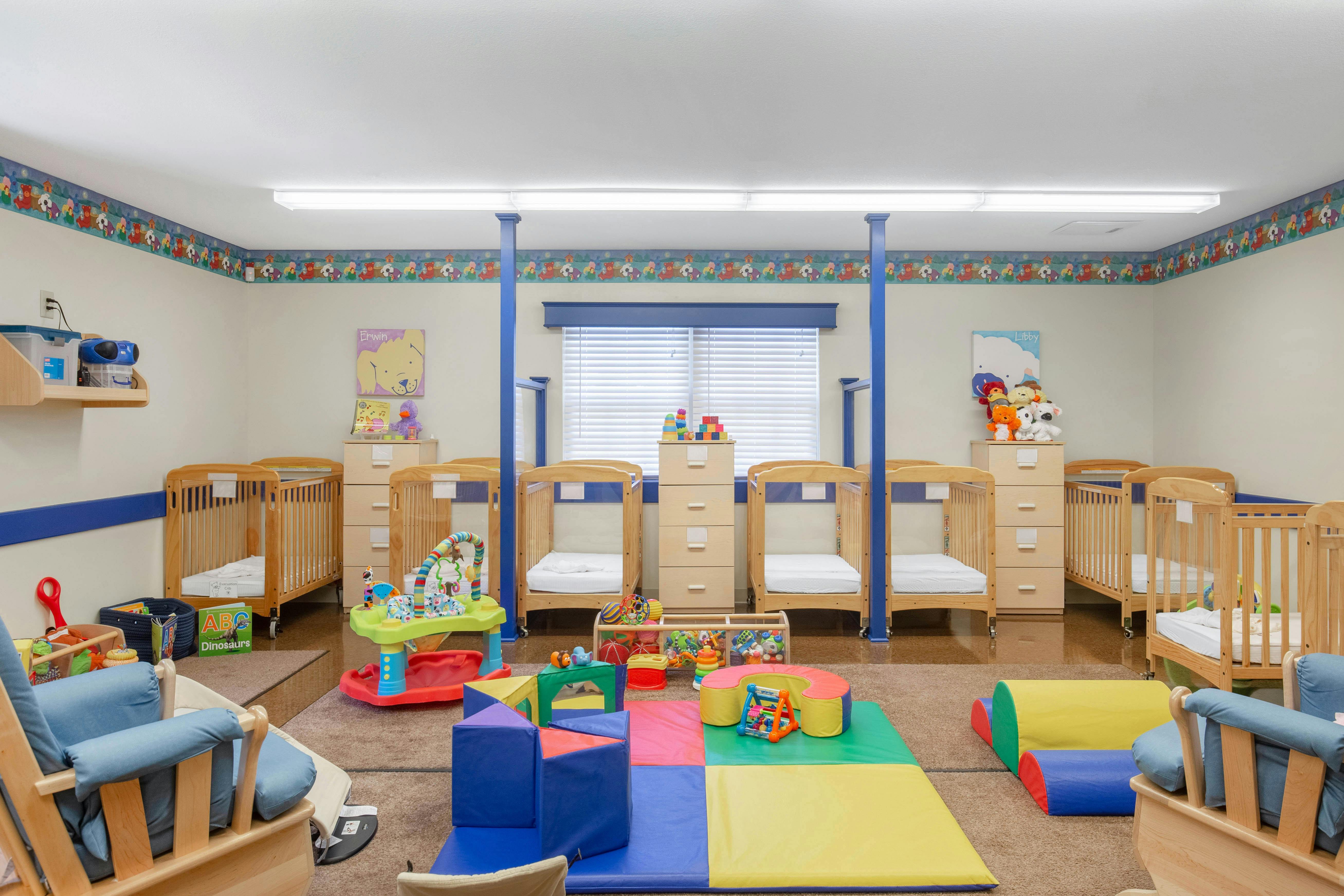 A brightly lit nursery with multiple cribs, changing tables, and colorful play mats