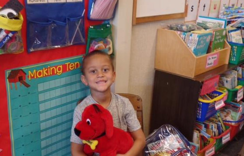 Child holding a red stuffed dog in a classroom