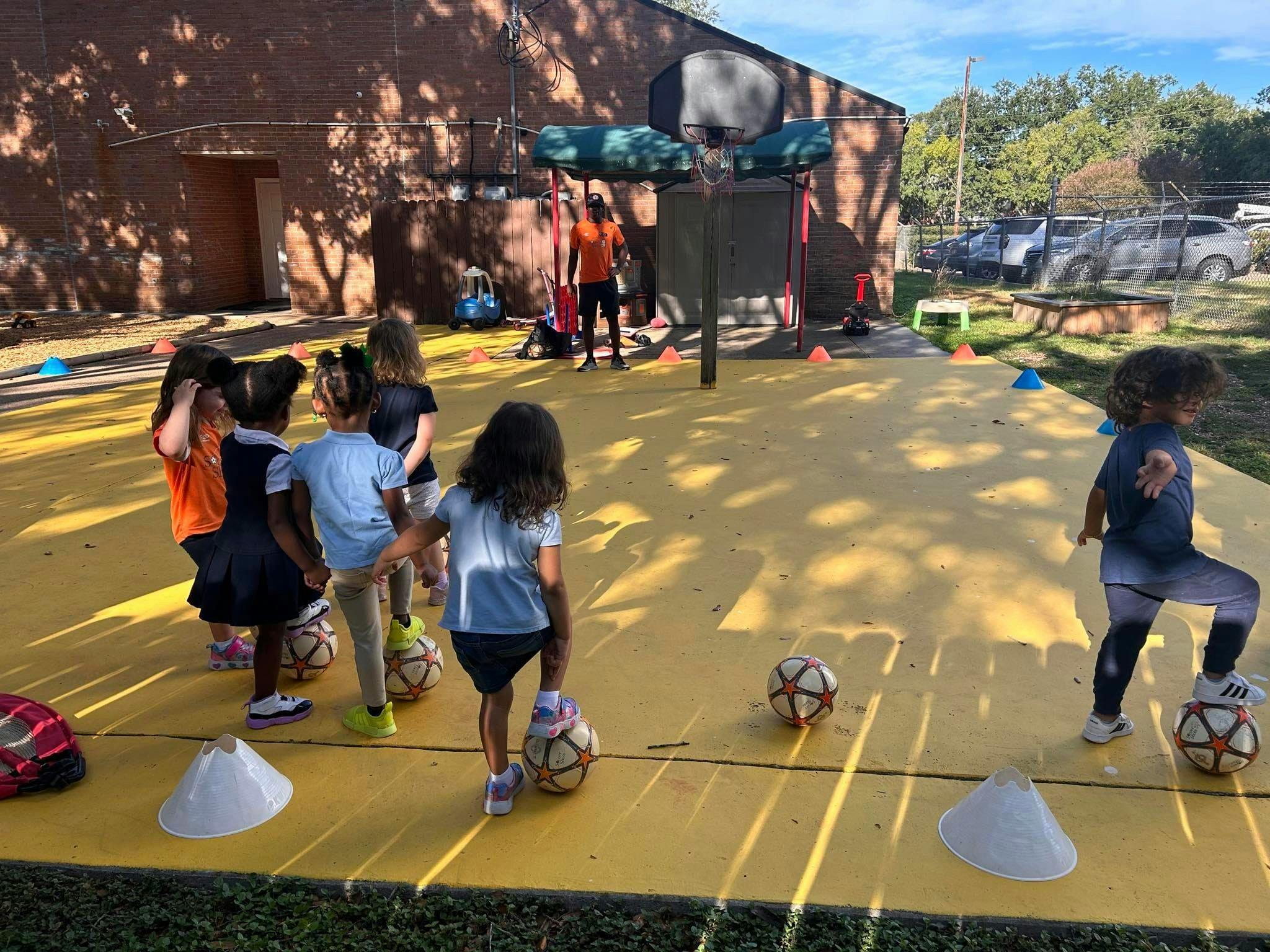 Children playing soccer on a yellow court with cones and an adult supervising