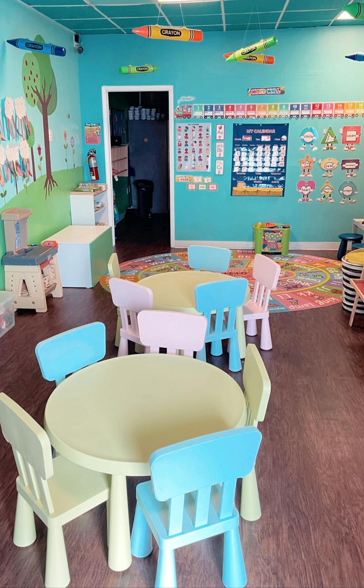 Classroom with small tables and chairs, colorful rug, and wall decorations