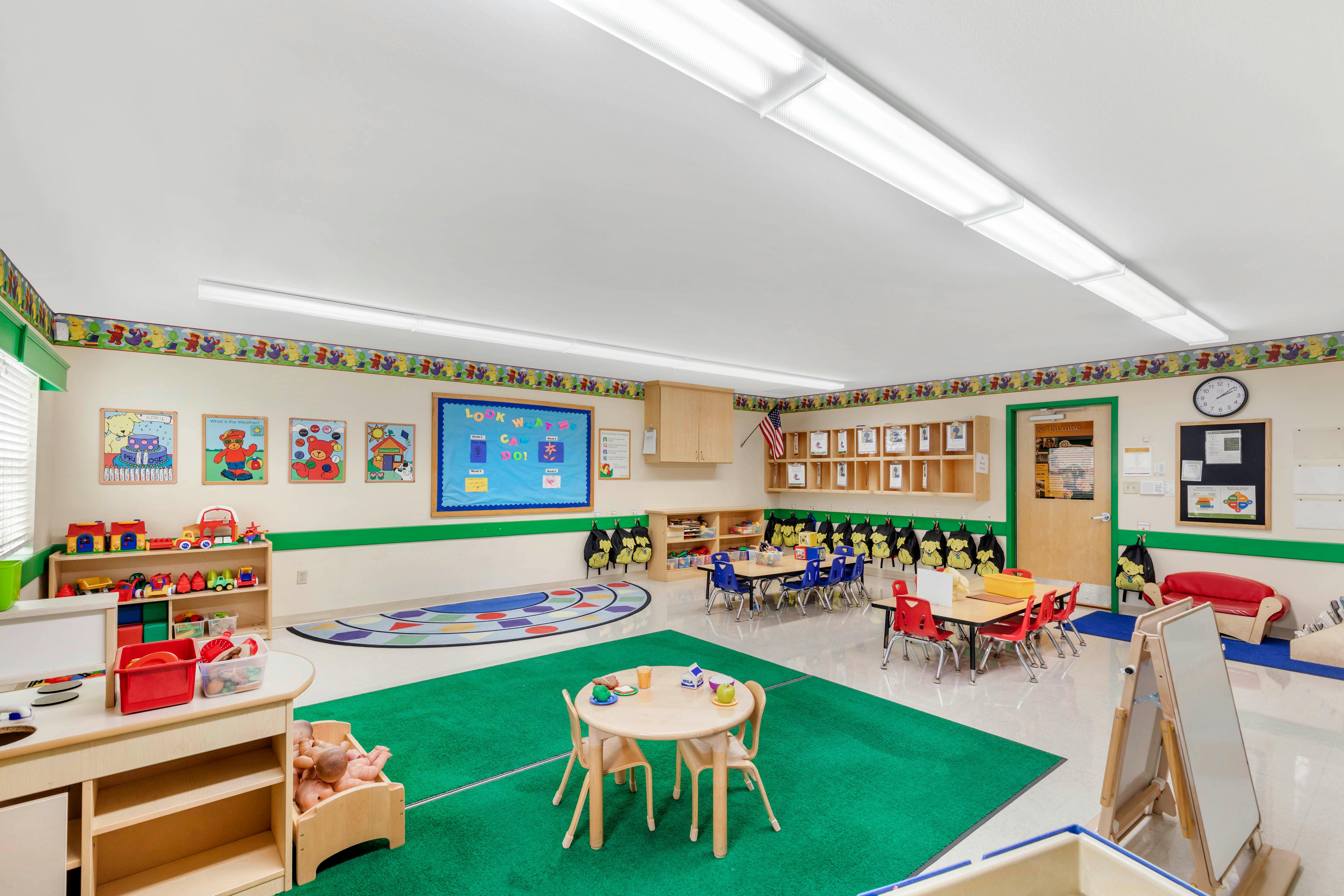 Bright classroom with small tables and chairs, toys, and colorful rugs