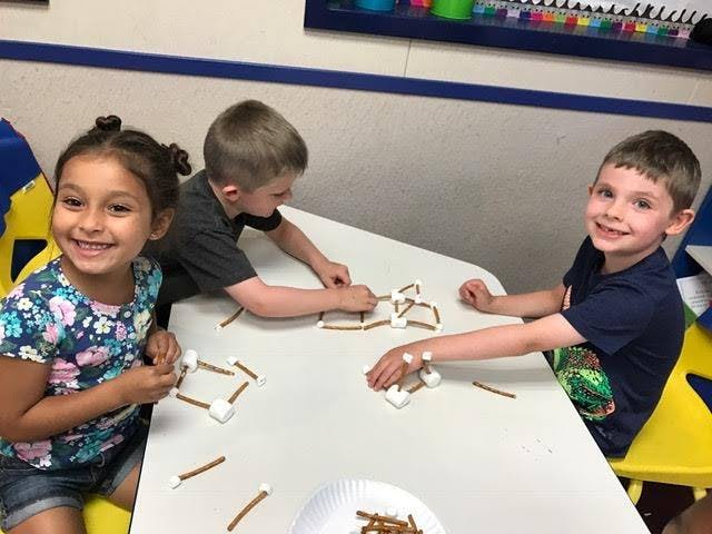 Three children at a table building with pretzels and marshmallows