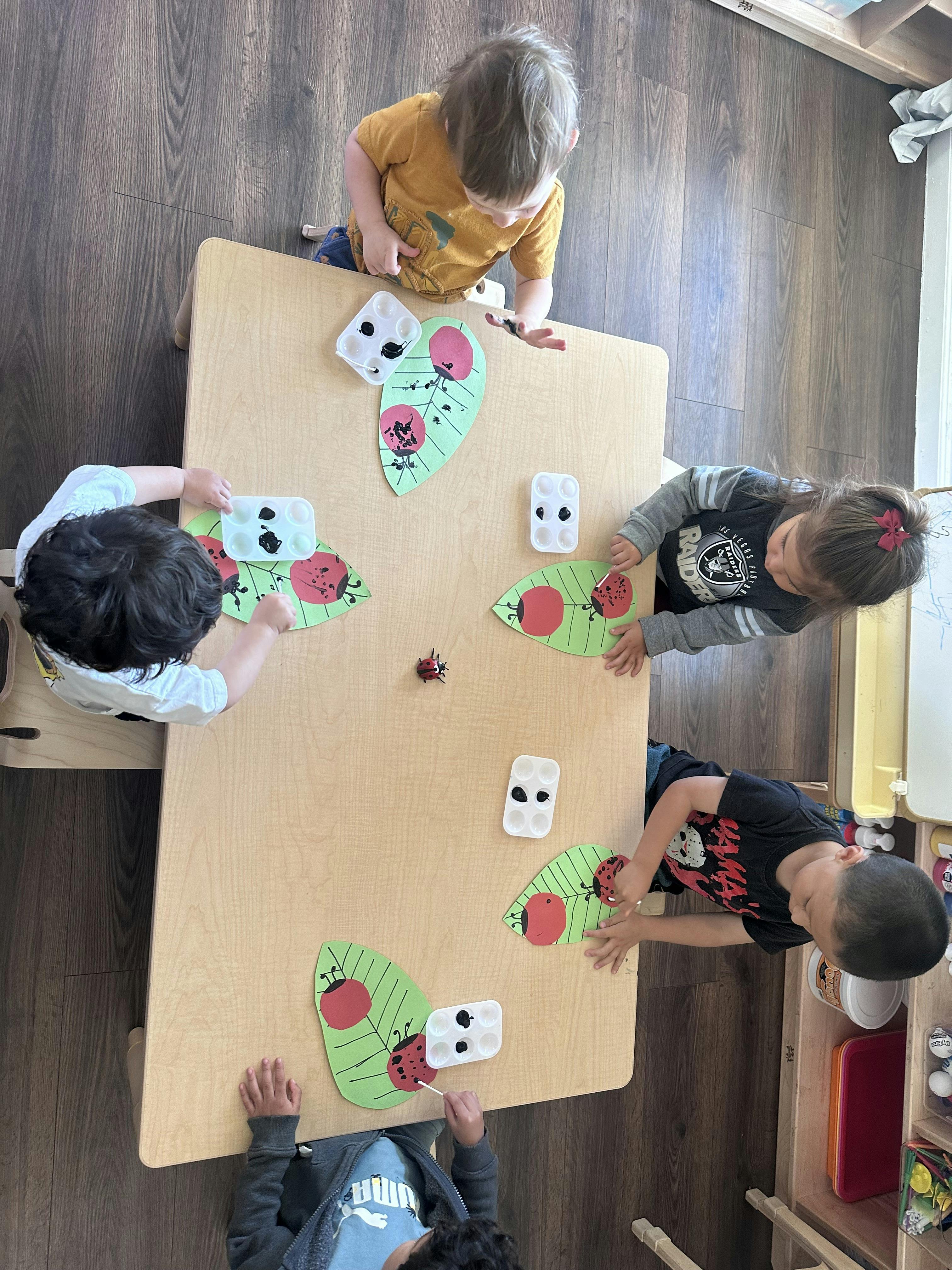 Children painting ladybugs on green paper leaves in a classroom