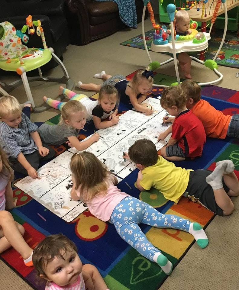 Children lying on a rug coloring on a large sheet of paper