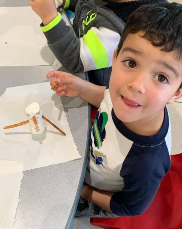 Child looking at camera with a marshmallow craft on the table