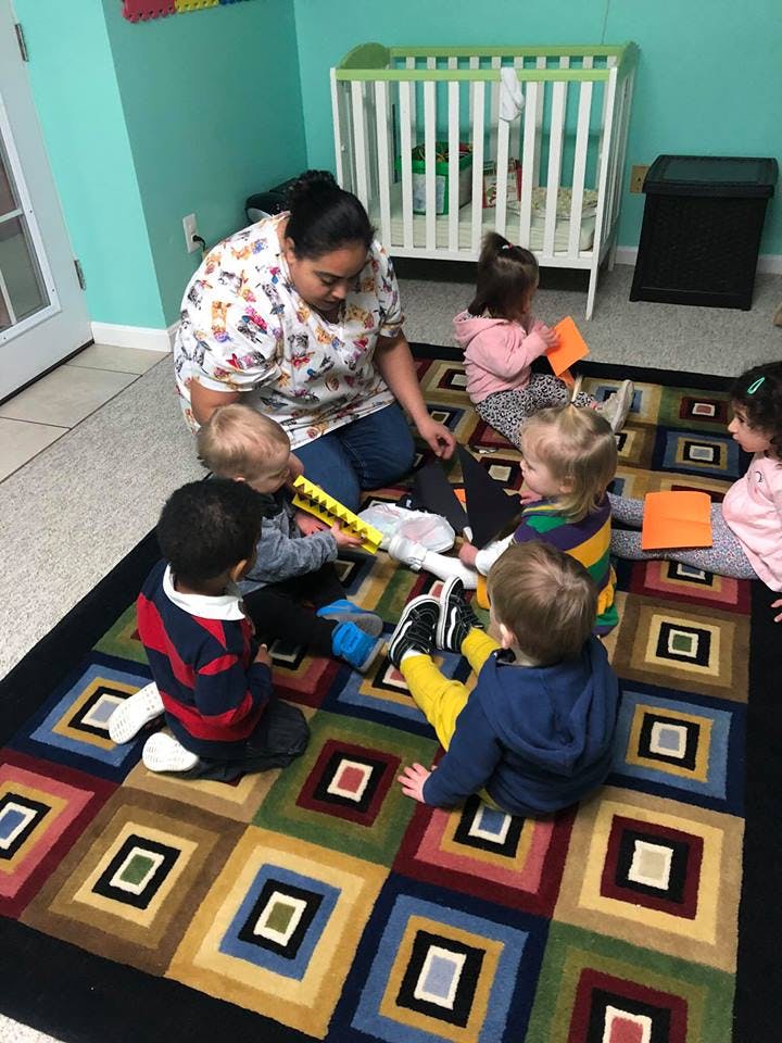 Person and multiple children sitting on a rug playing with toys