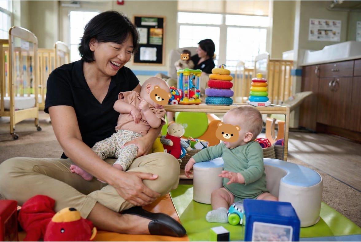 Smiling person holding one baby and another baby sitting on the floor