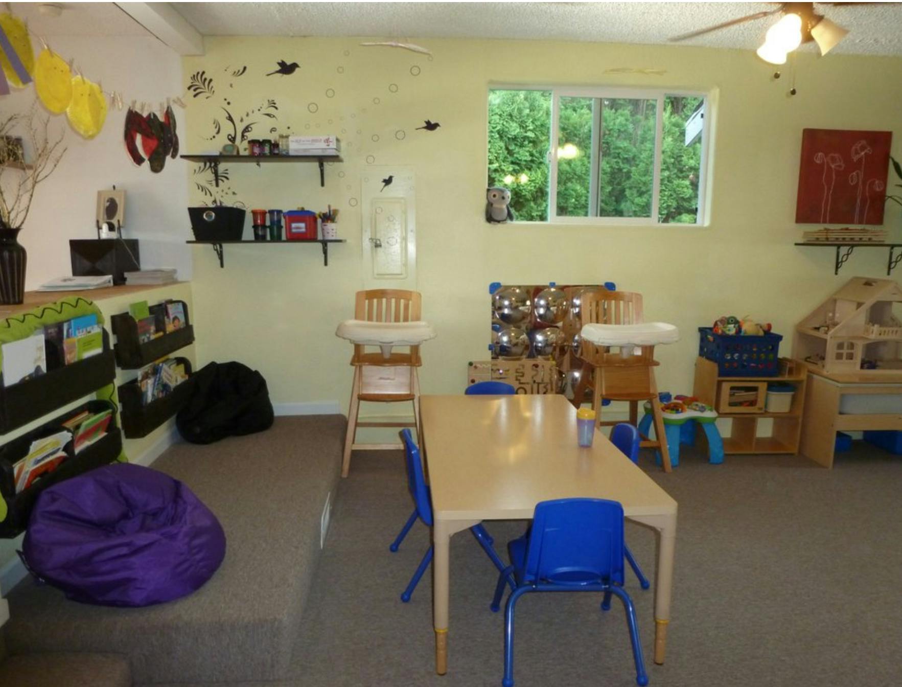 Childcare room with small tables and chairs, high chairs, and toys