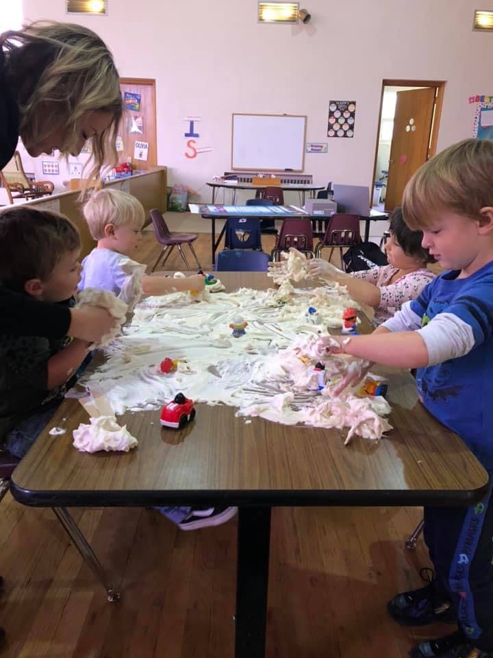 Adult and children playing with a messy substance on a table in a classroom