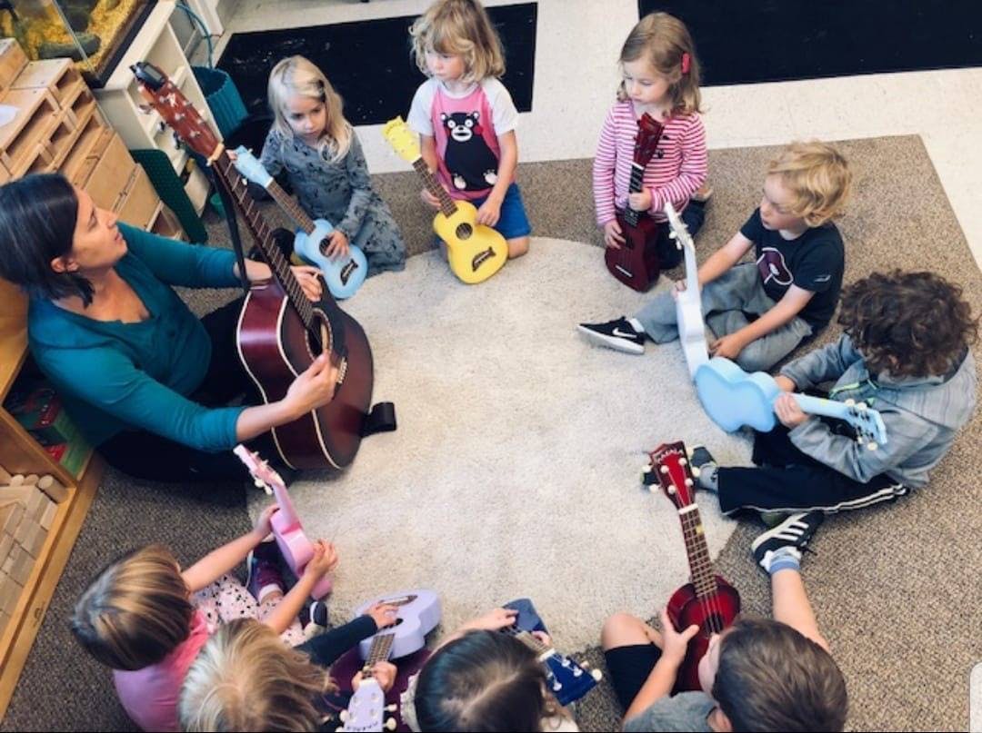 Person playing guitar with children playing ukuleles in a circle