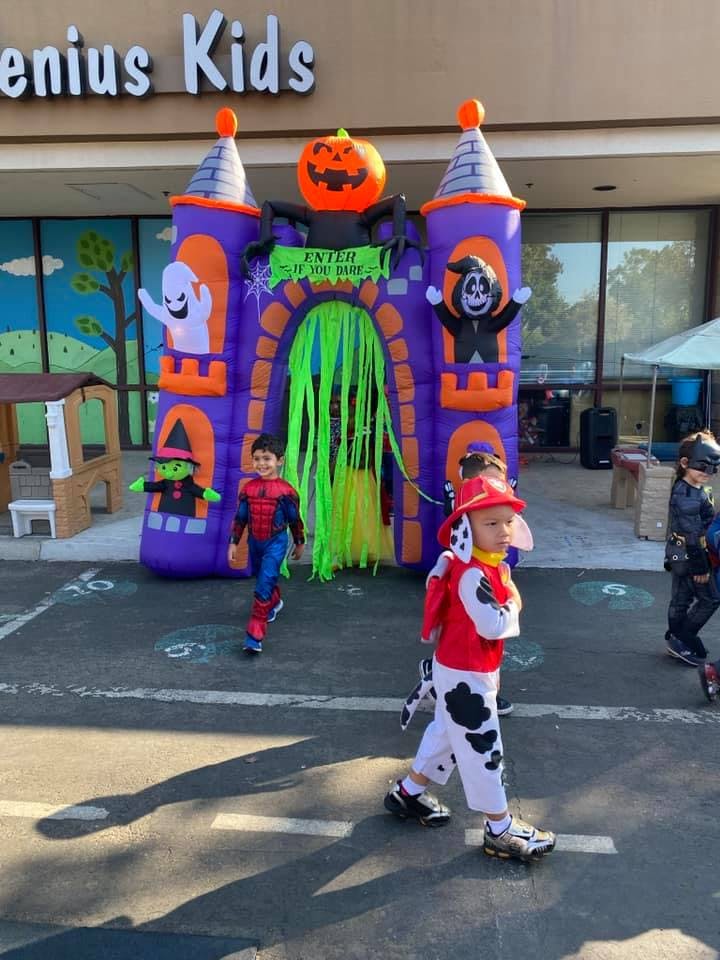 Children in costumes walking past a Halloween-themed inflatable bounce house