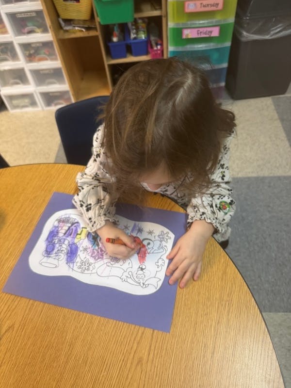 Child coloring a picture on a purple sheet at a table