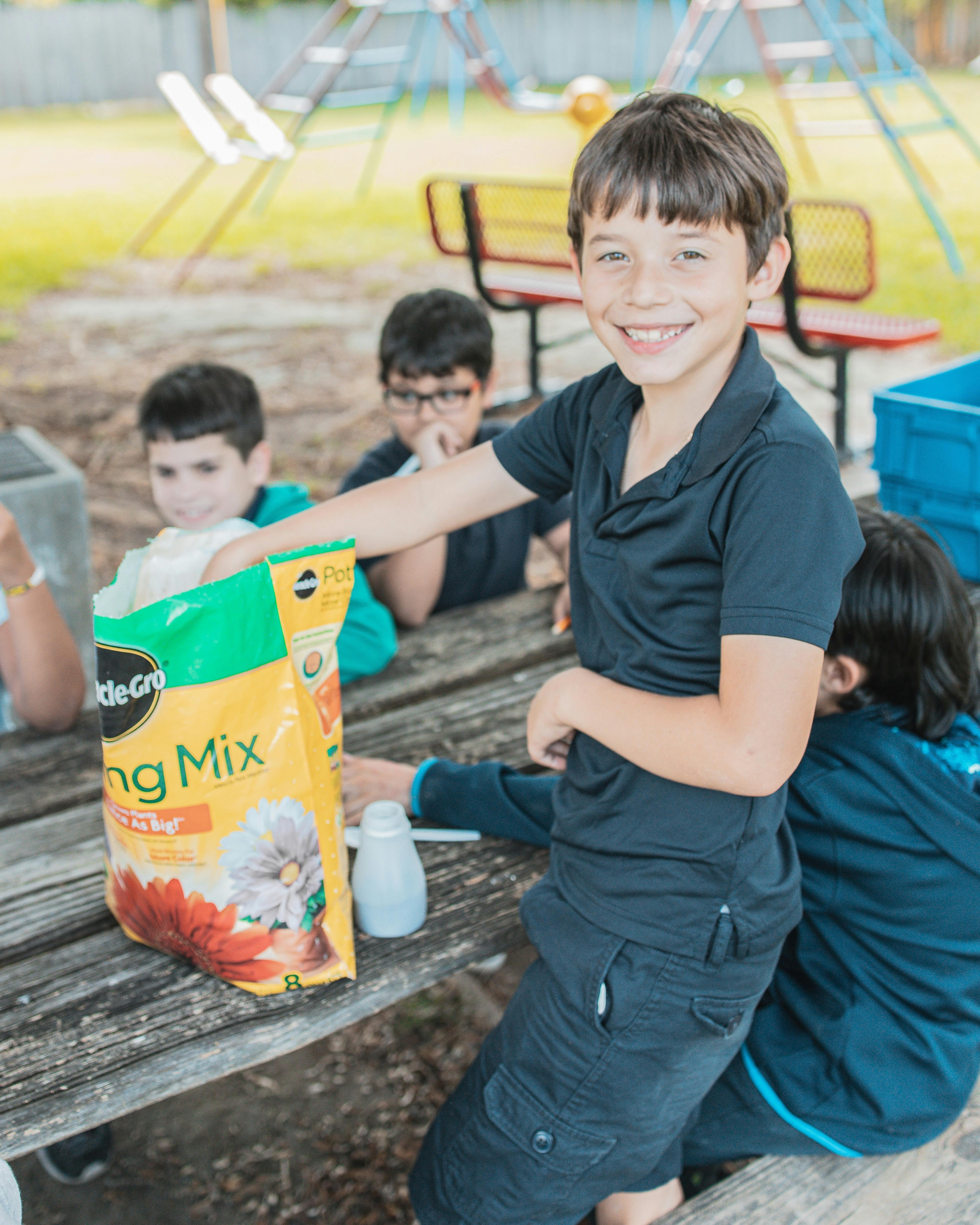 Child reaching into a bag of potting mix at an outdoor table