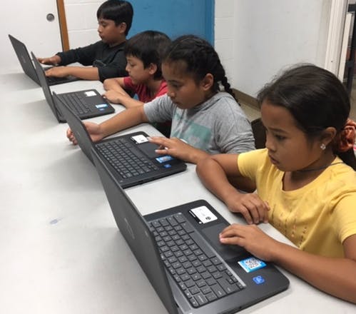 Four children sitting at a table using laptops
