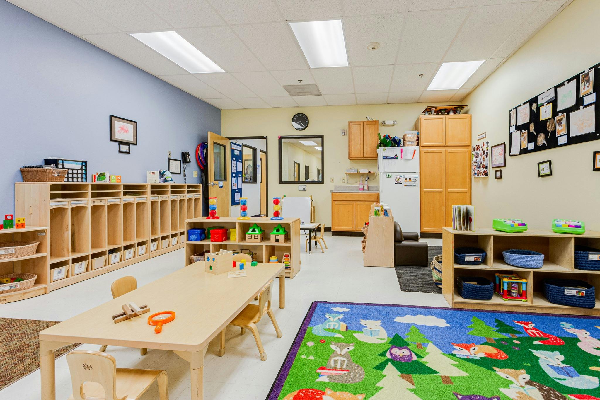 Empty classroom with small tables and chairs, cubbies, and a colorful rug