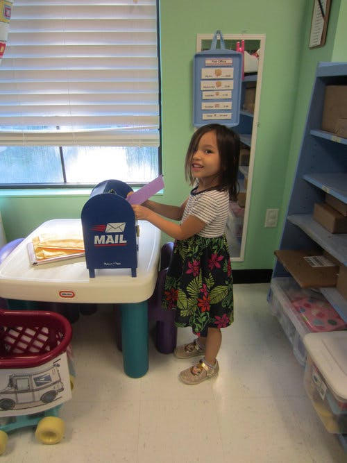 Child putting a letter into a toy mailbox in a classroom