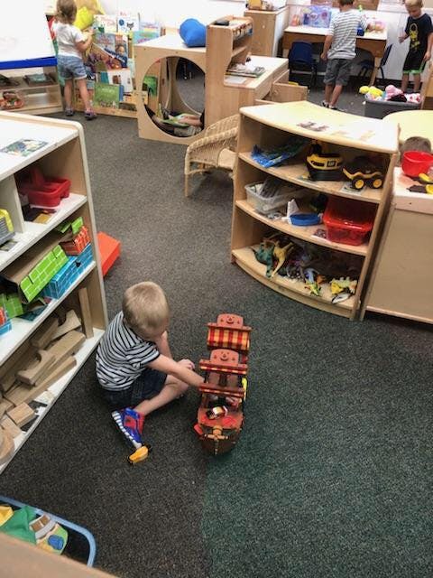 Child playing with a toy boat on the floor in a classroom