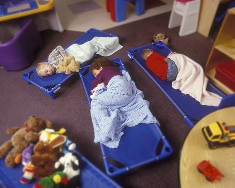 Three children sleeping on cots in a room