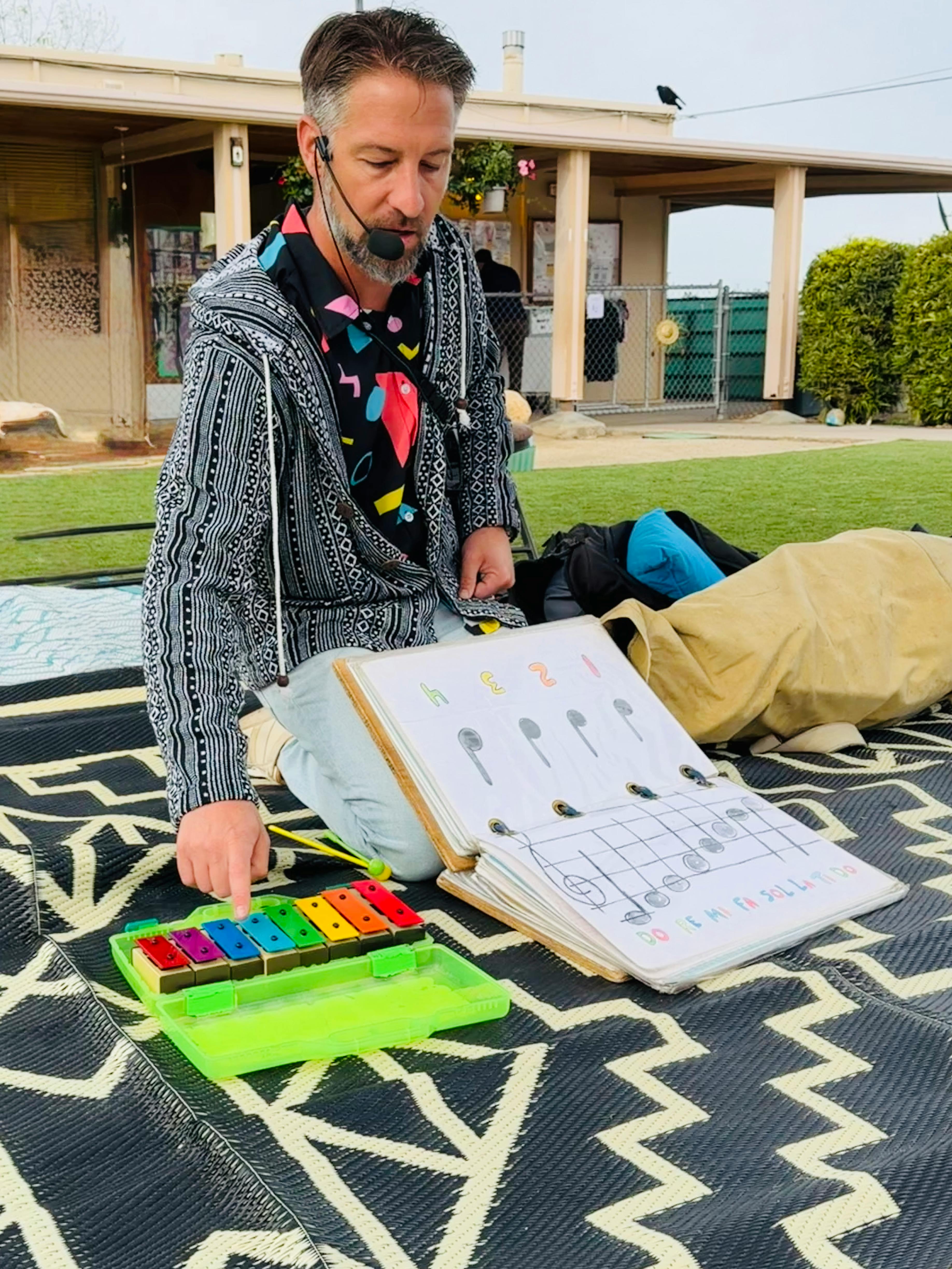 Person playing a small xylophone next to a music notation book on a rug