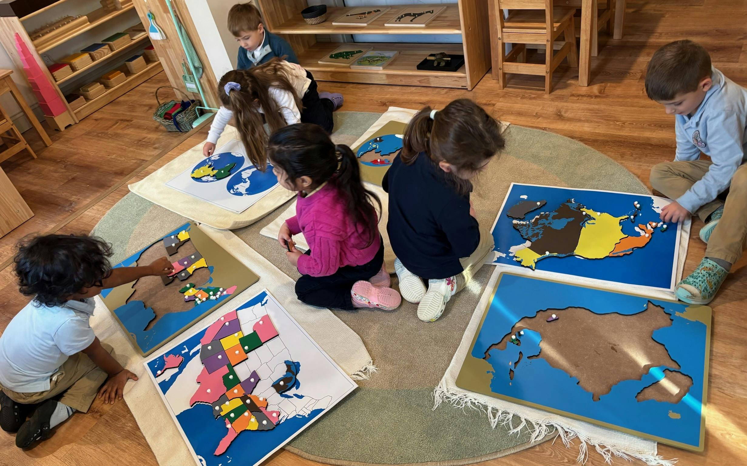 Several children in a classroom assembling map puzzles on the floor