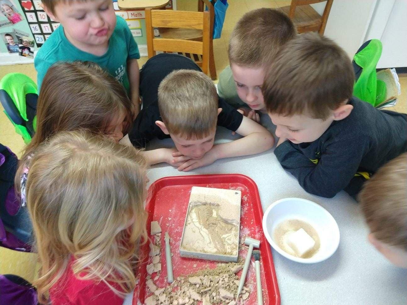 Children gathered around a table looking at a tray with a fossil excavation kit