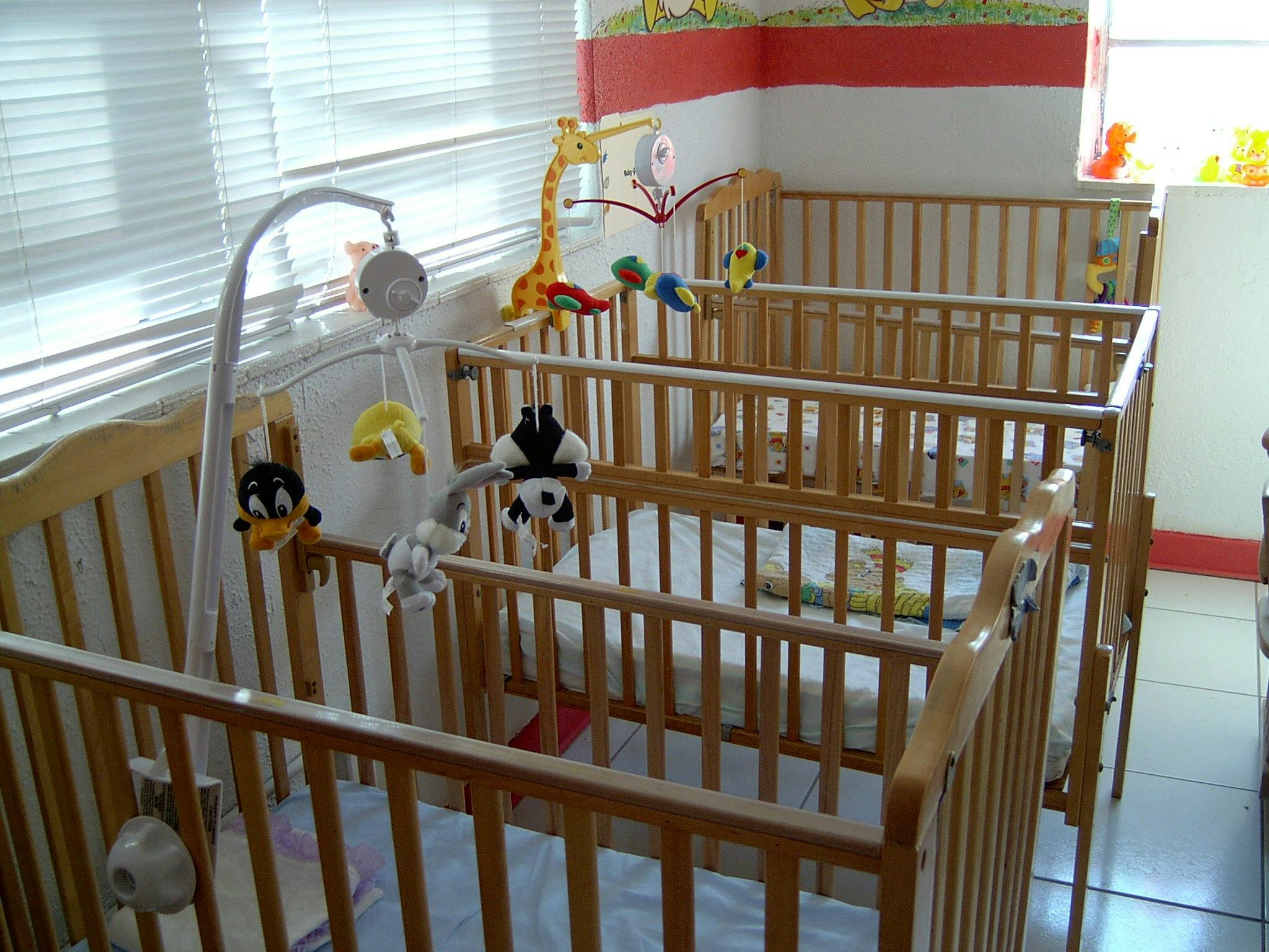 Multiple empty wooden cribs with mobiles in a room