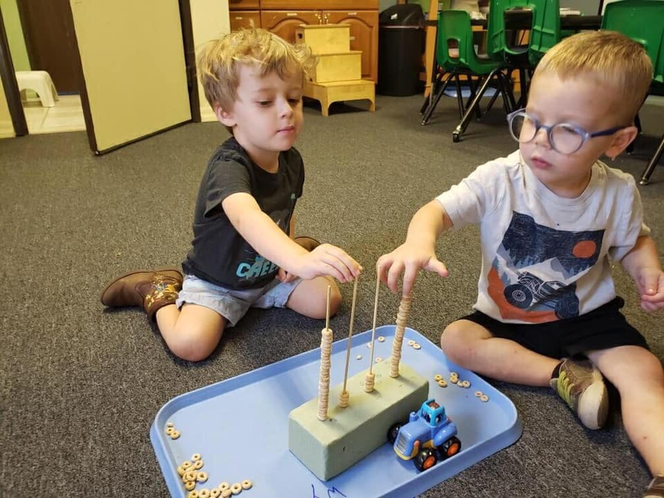 Two children playing with a pegboard and small pieces on a tray