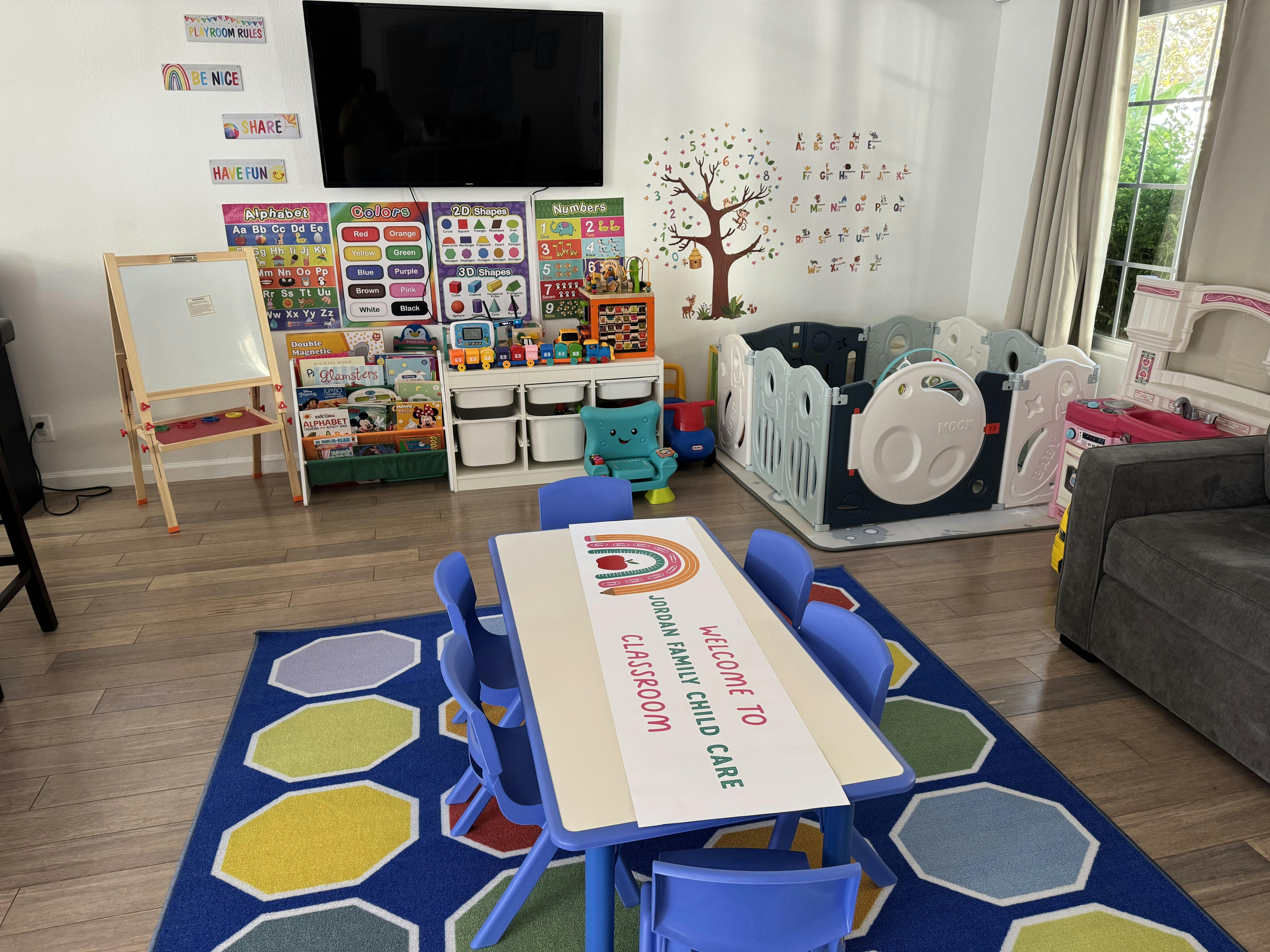 A classroom with a small table and chairs, playpen, and learning posters