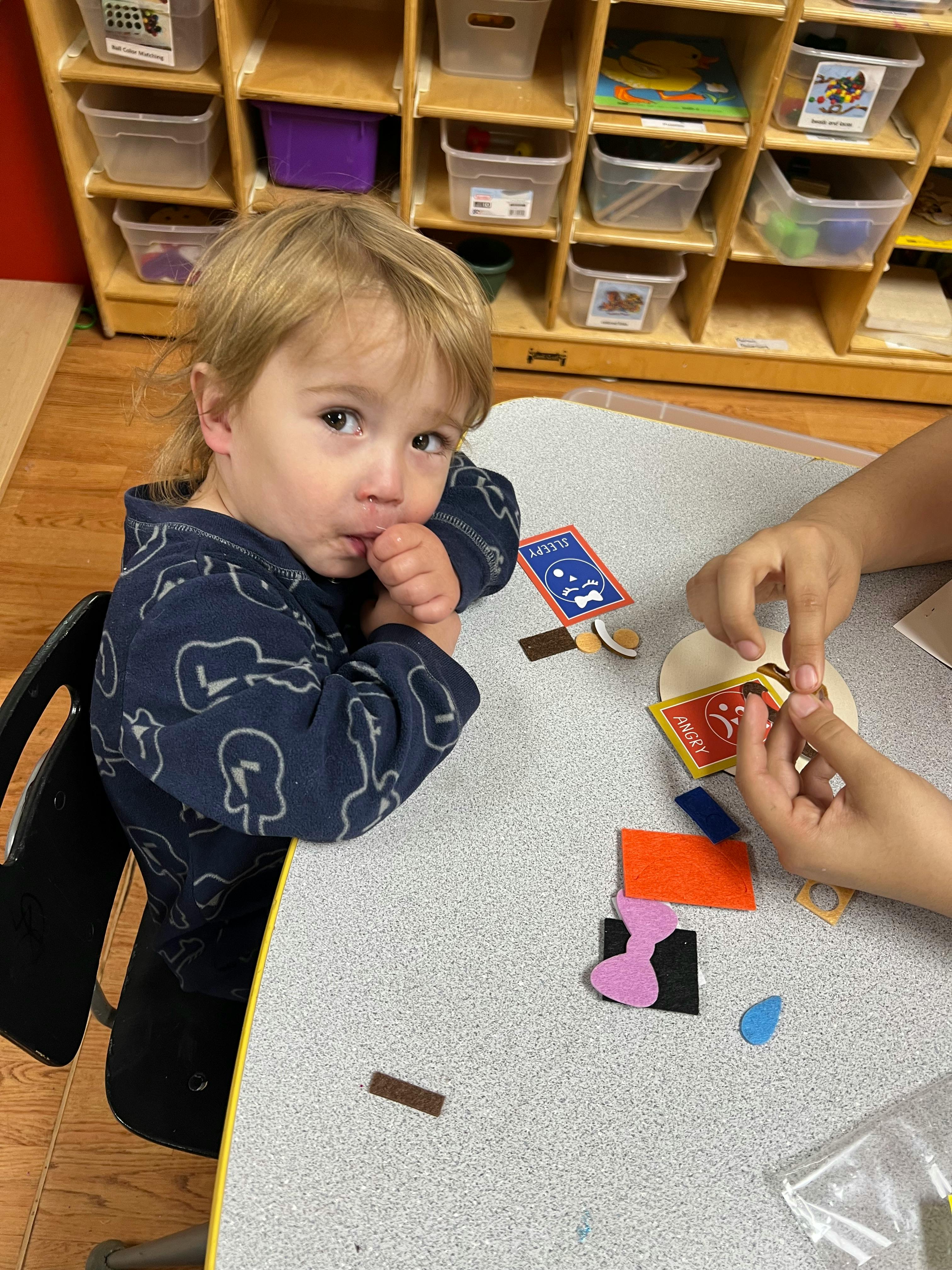 Child sitting at a table with another person's hands, crafting with craft materials