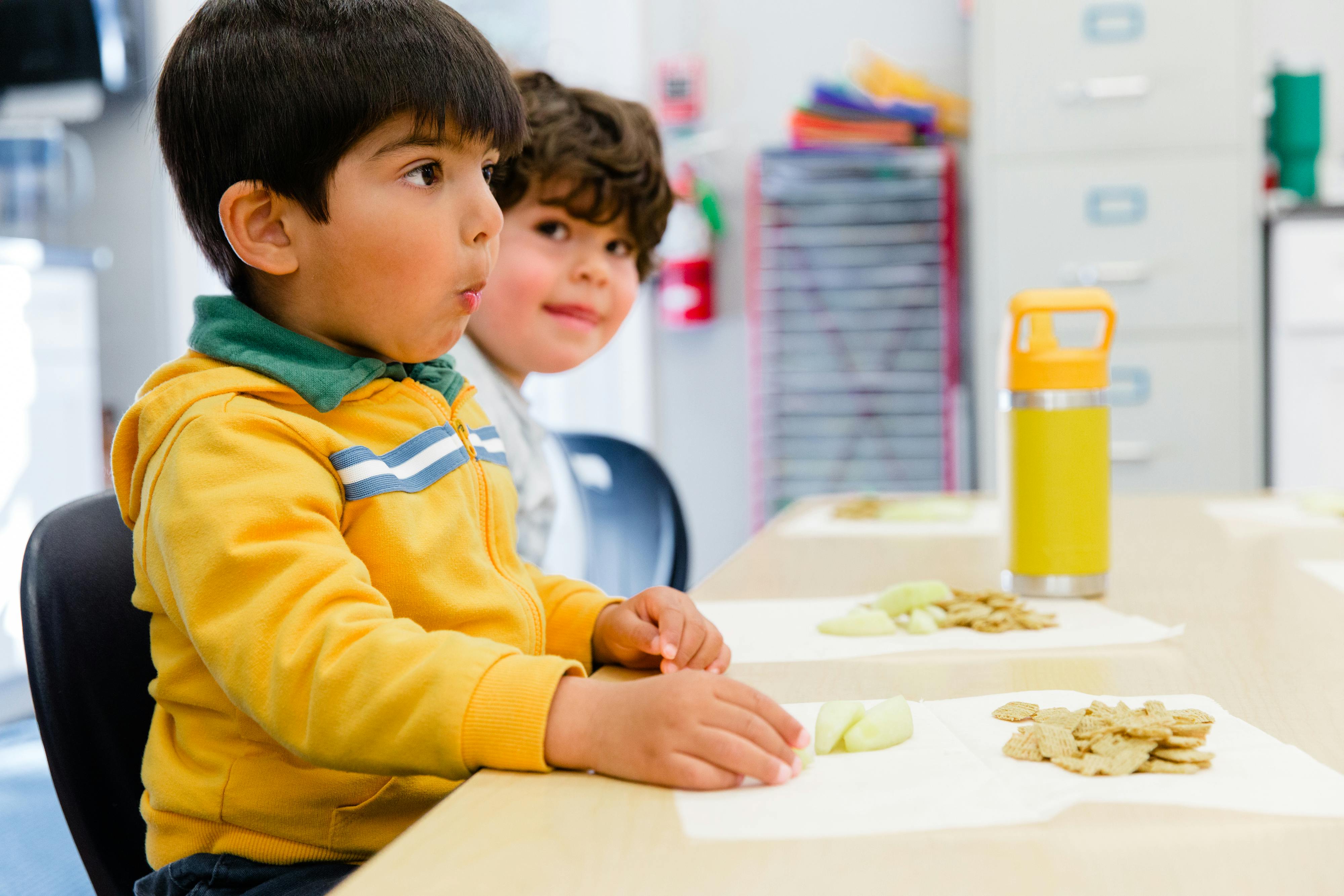 Two children sitting at a table with snacks