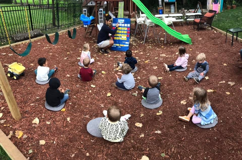 Adult teaching a group of children sitting on the ground outdoors