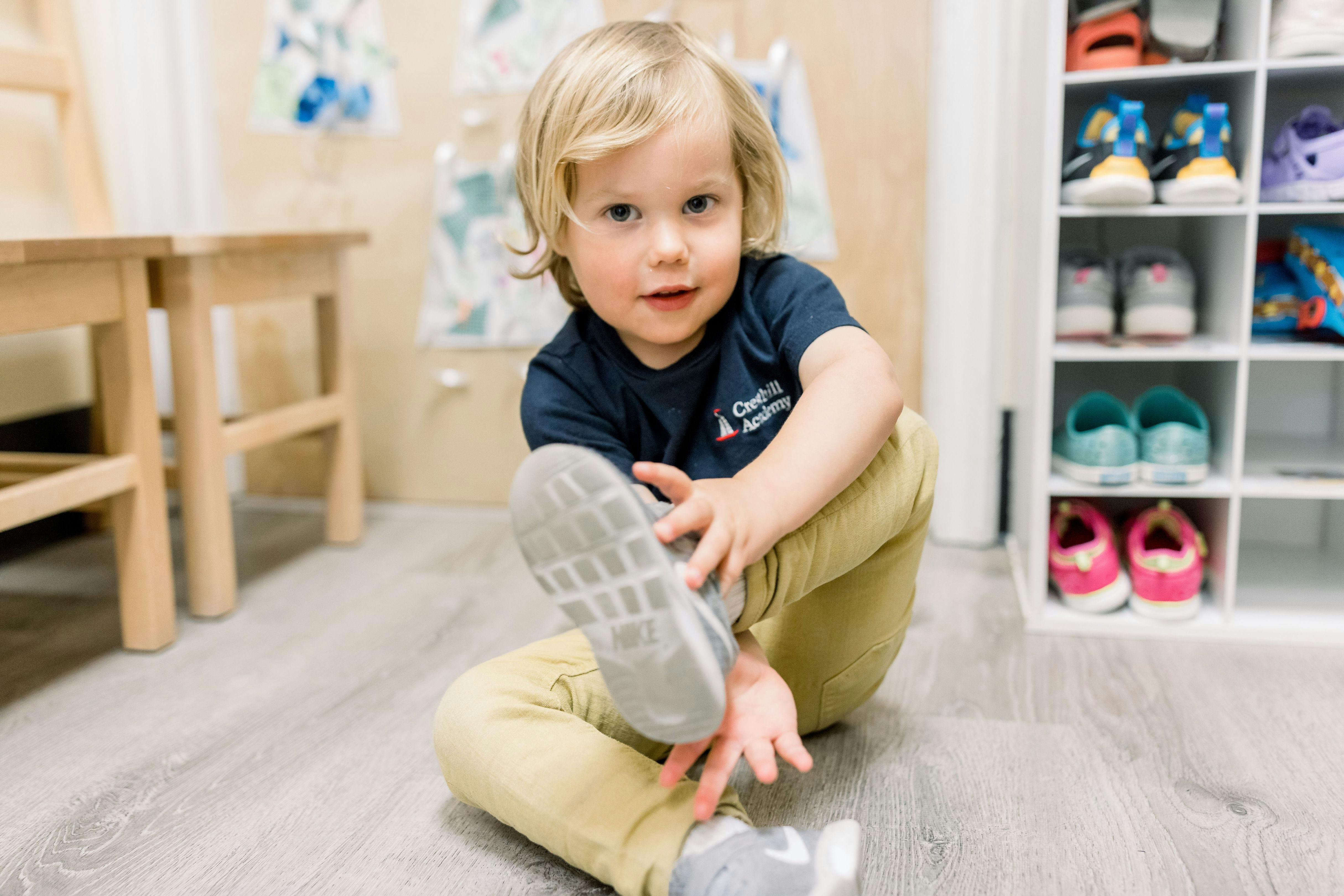 Child sitting on a classroom floor putting on a shoe