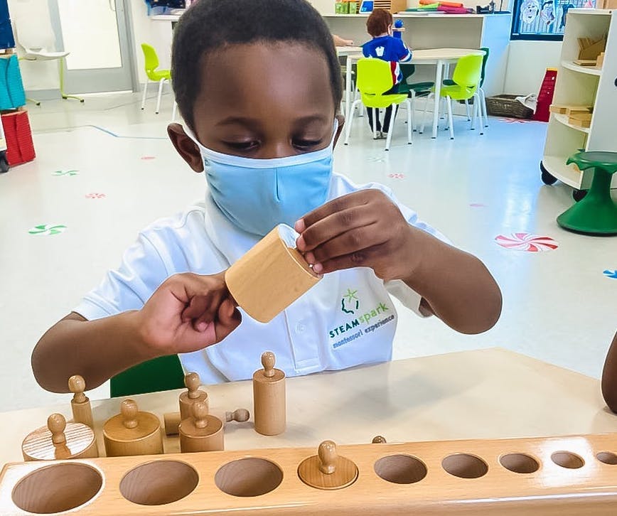 Child in mask playing with wooden cylinder blocks