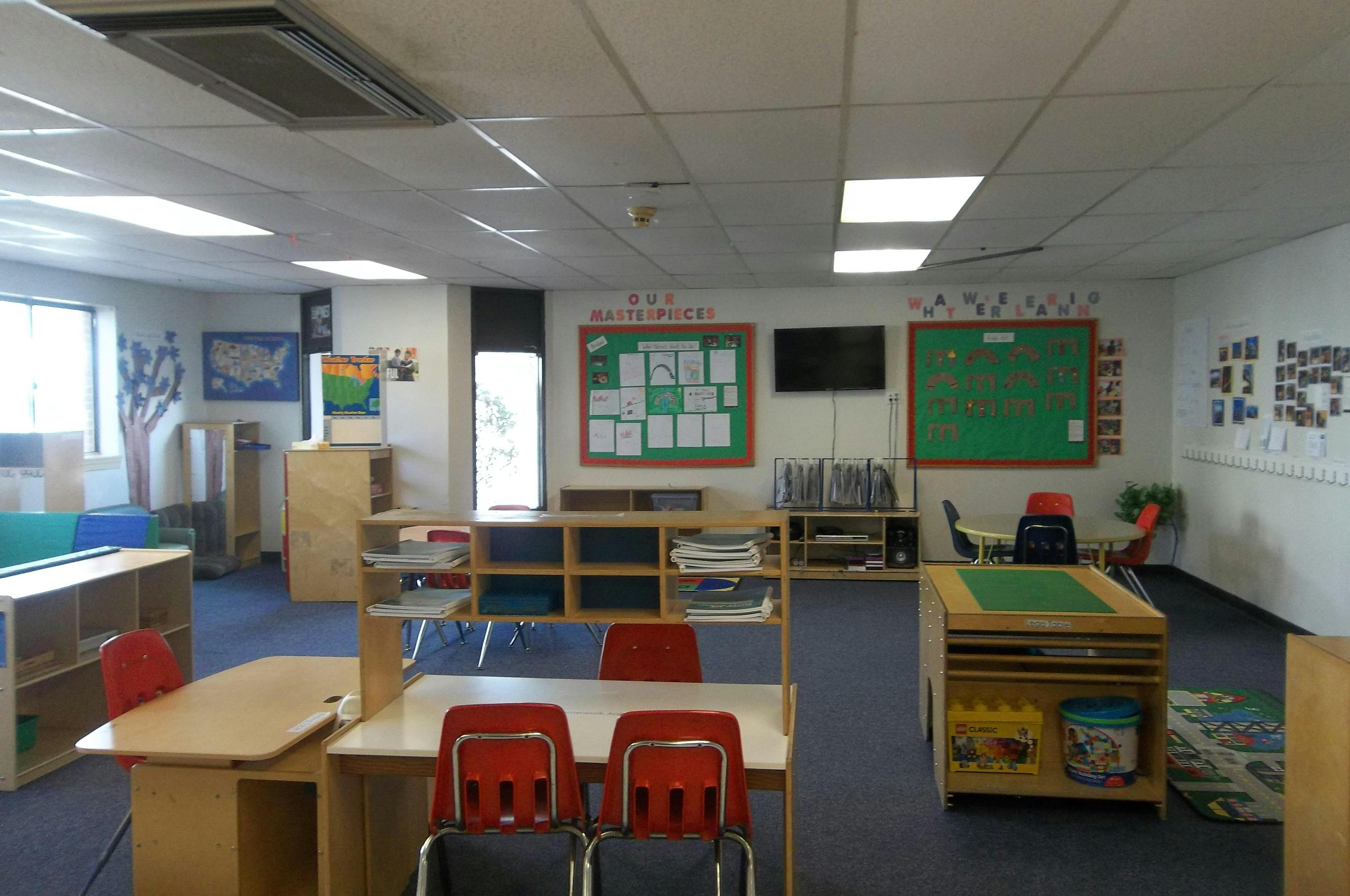 An empty classroom with desks, chairs, storage cubbies, and bulletin boards