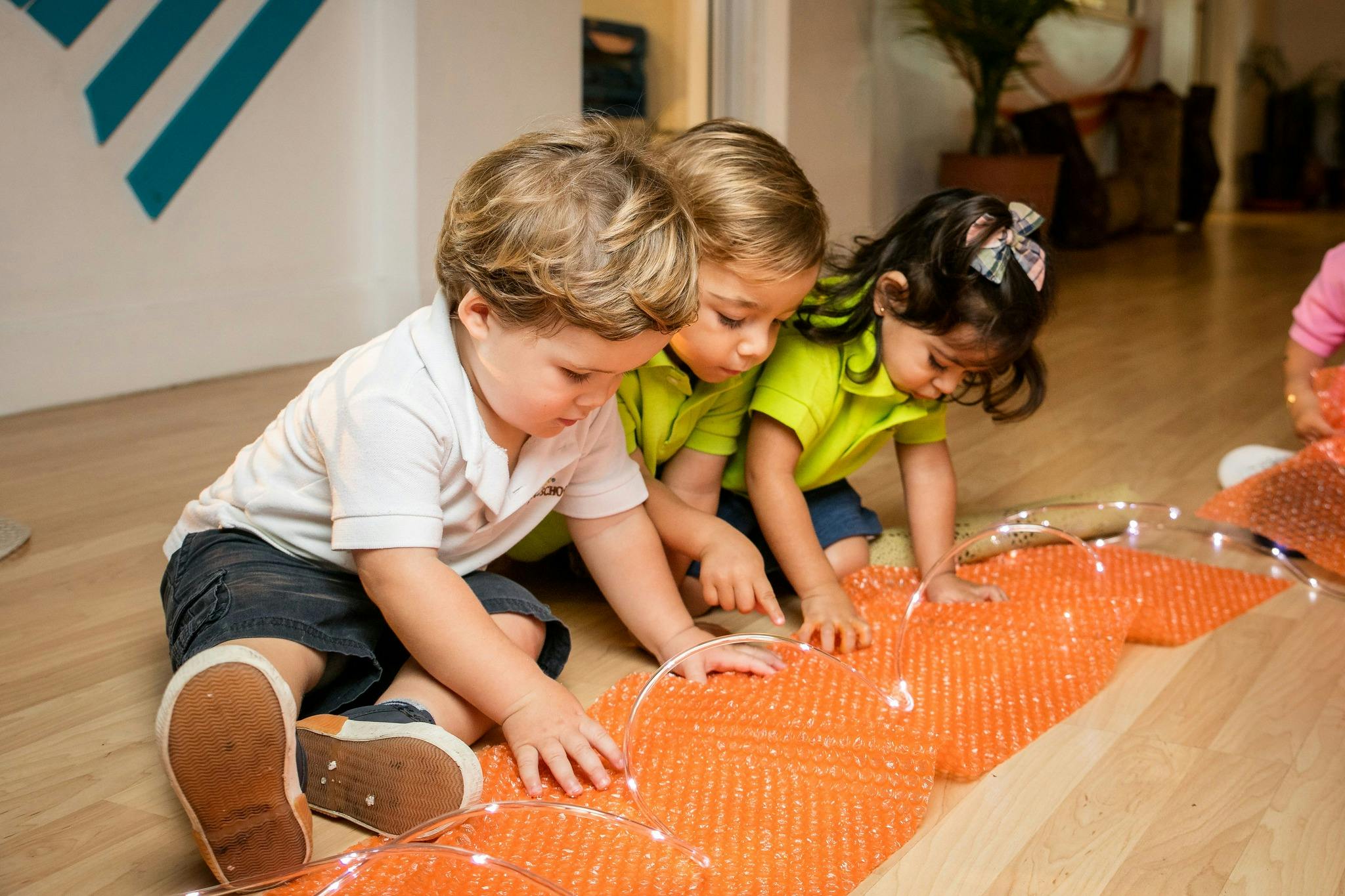 Three children on the floor touching an orange textured mat with lights