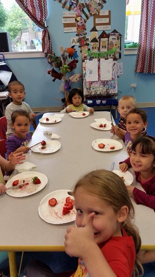 Children sitting at a table with plates of strawberries