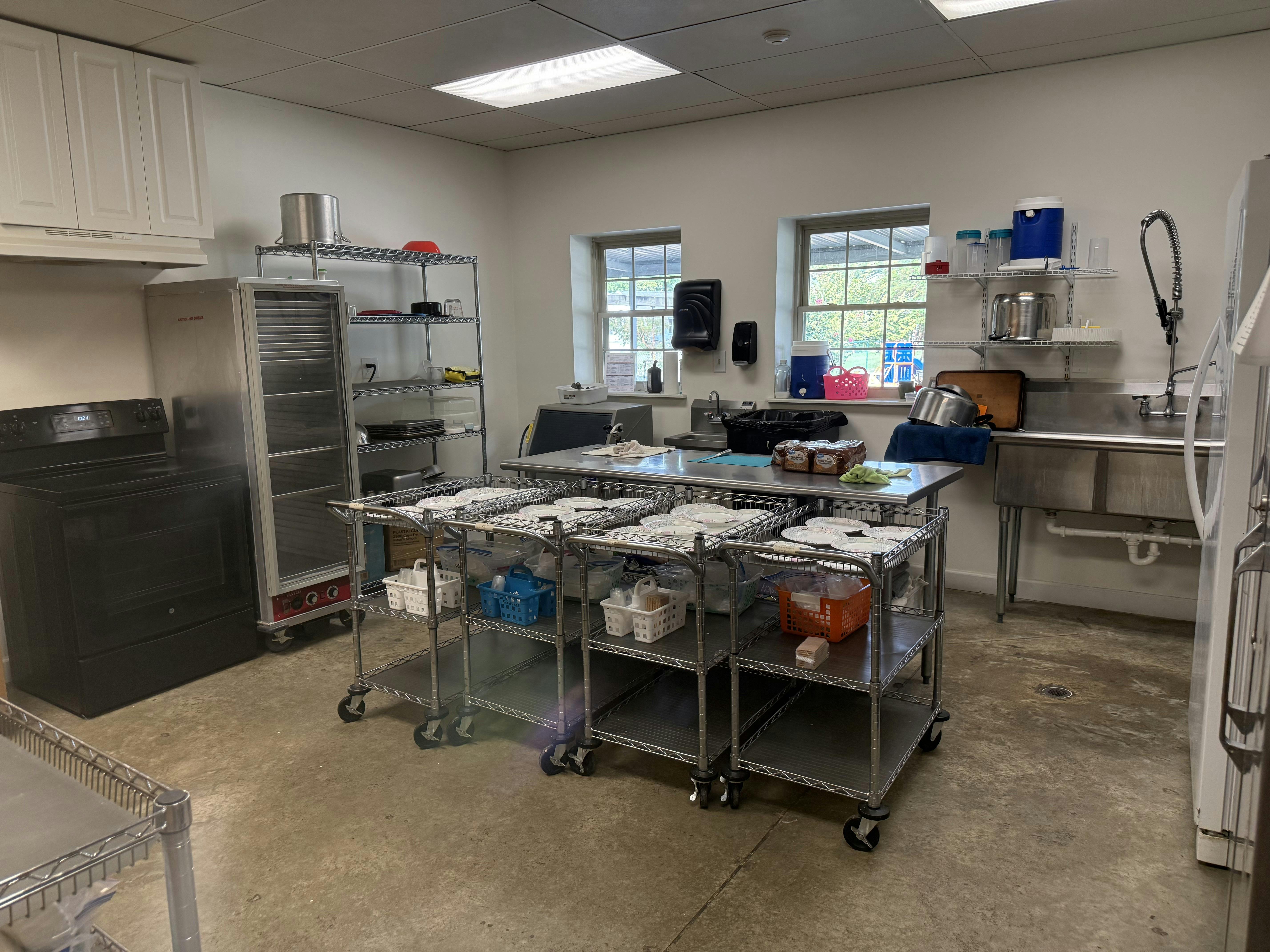 Commercial kitchen with metal prep tables and rolling carts holding dinnerware