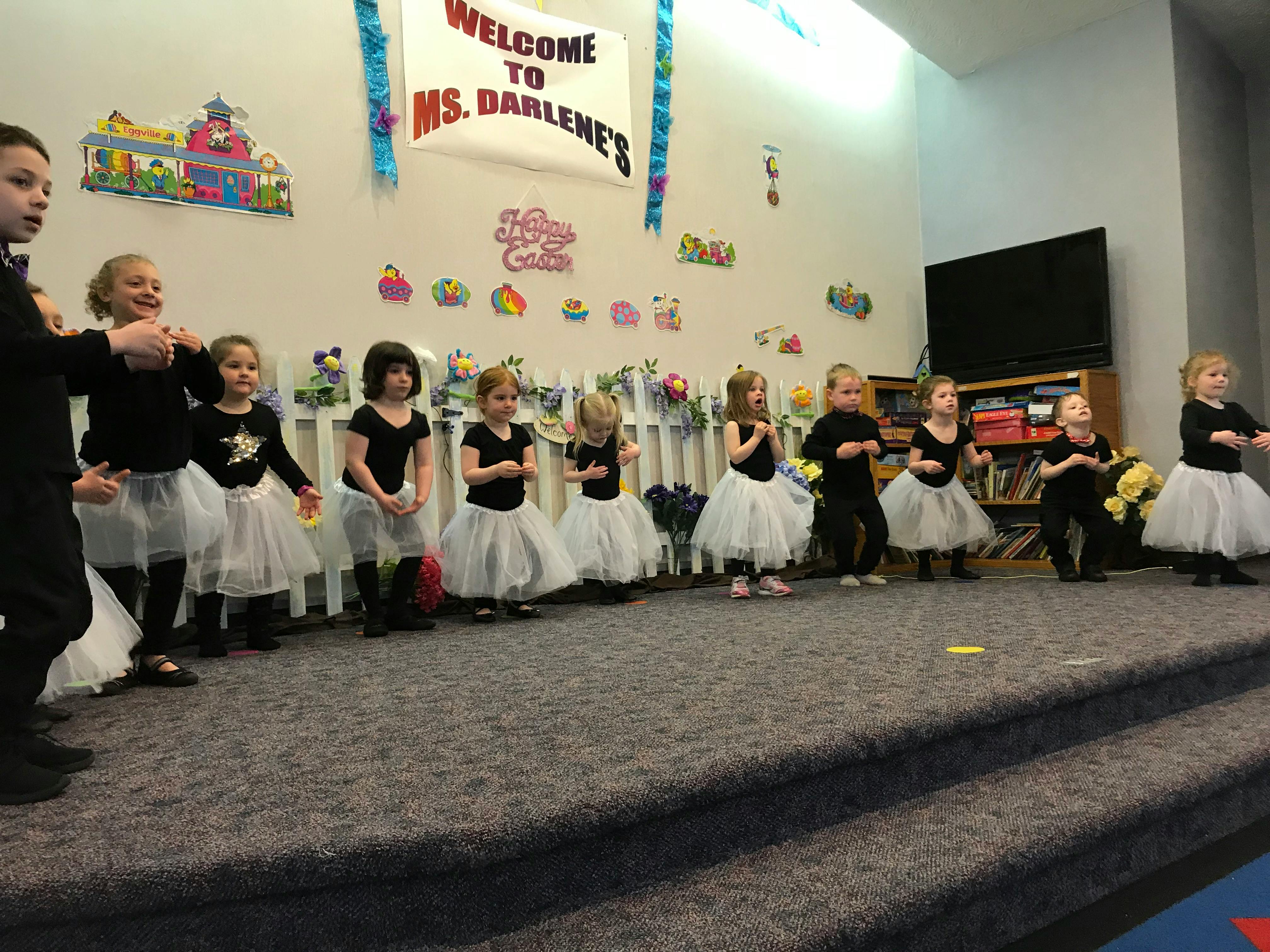 Children in black shirts and white tutus standing on a stage