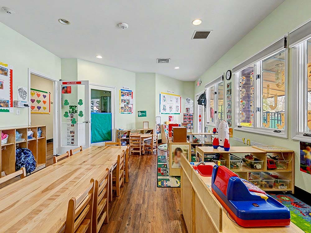 Empty classroom with long wooden tables, chairs, and learning materials