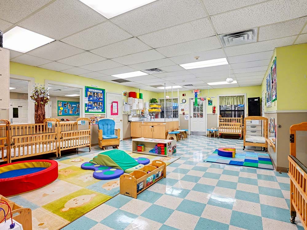 Empty colorful daycare room with cribs, playmats, and small furniture
